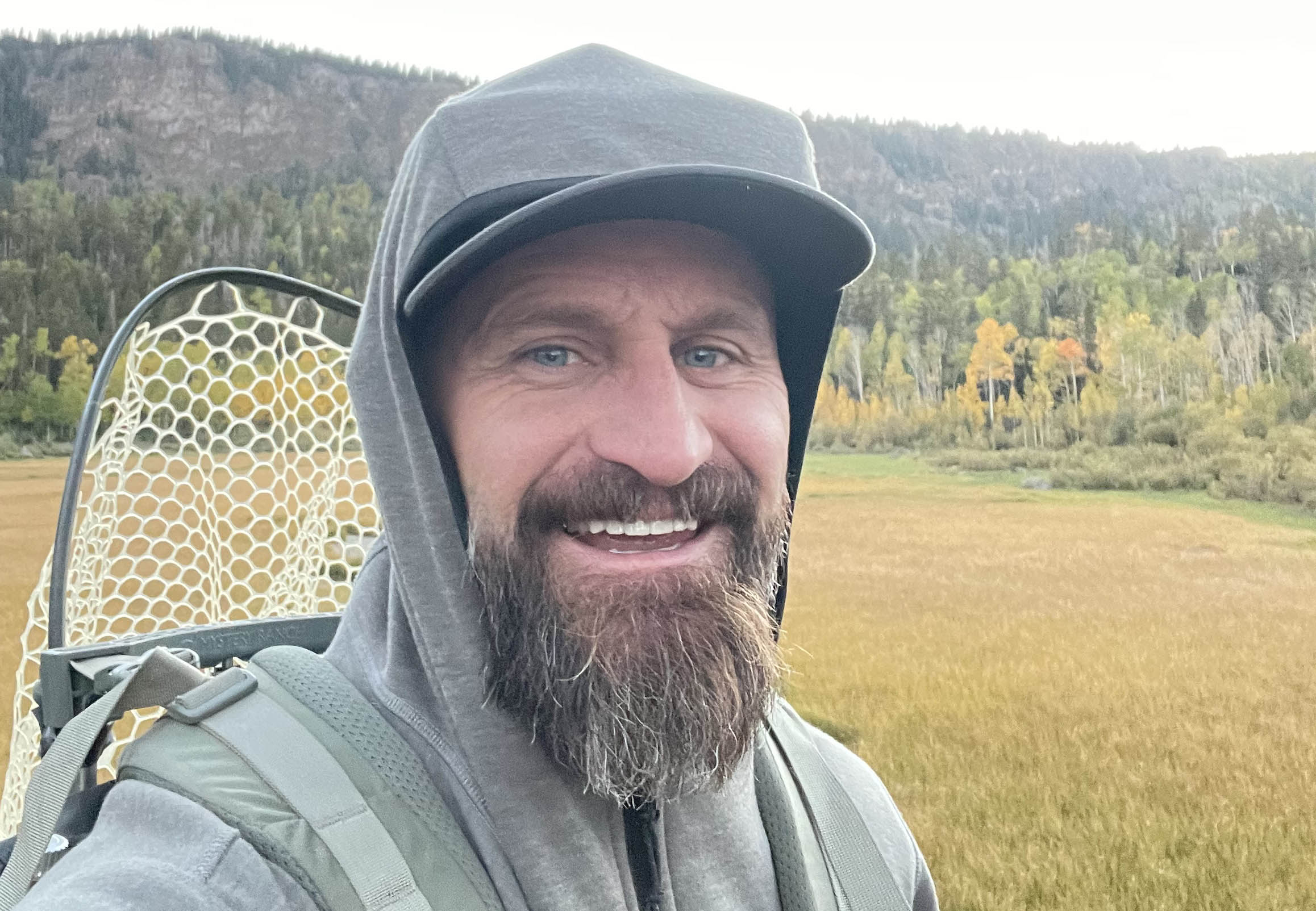 Matt Smith on the trail with a fishing net, mountain meadow behind him
